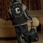 A child in a fashionable hooded jacket and jeans with a bag indoors.