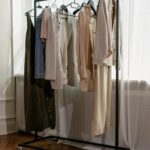 A minimalist clothing rack with neutral outfits and white sneakers in a bright room.